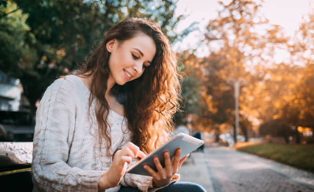 istock Joyful girl in autumn scenery using digital tablet outdoors browsing internet 1205495857