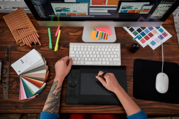 istock Professional web illustrator. Top view of a graphic designer using graphic tablet and computer in the office or studio. Workplace with graphic tablet, keyboard, computer and color swatches 1205496099