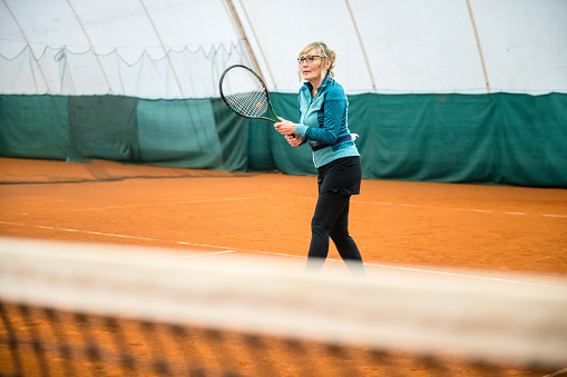 Senior Woman Playing Tennis in indoor tennis court.