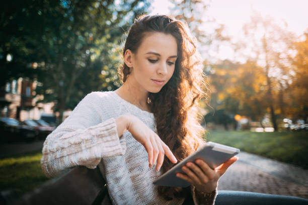 istock Joyful girl in autumn scenery using digital tablet outdoors browsing internet 1205499838