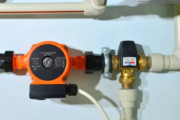 Pump with a thermometer for a water underfloor heating system at home. Sensor and temperature control. Manometer, pipe, flow meter, and valves of heating system in a boiler room.