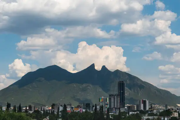 The iconic Cerro de la Silla in the northern Mexican city of Monterrey, on a bright cloudy day. A couple of buildings can be seen on the horizon.