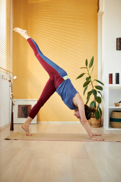 istock Attractive fit caucasian middle aged brunette doing Three Legged Downward-Facing Dog yoga pose in the morning. Home interior. 1205501098
