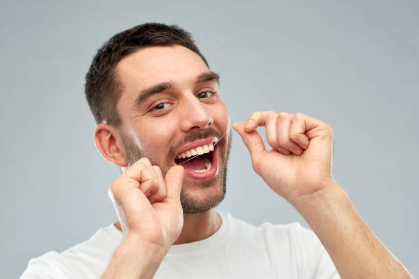 istock man with dental floss cleaning teeth over gray 1205501302