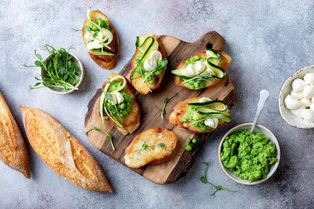 istock Appetizer crostini with mashed green pea, mozzarella, pea sprouts and zucchini ribbons on wooden board. Delicious healthy snack, spring appetizers 1205503702
