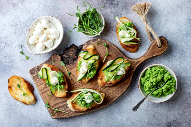 istock Appetizer crostini with mashed green pea, mozzarella, pea sprouts and zucchini ribbons on wooden board. Delicious healthy snack, spring appetizers 1205503755
