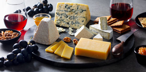 istock Cheese assortment on dark marble cutting board with red wine. Grey background. 1205503878