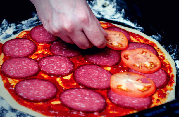 aplicação de tomates na massa de pizza. cozinhando pizza. o cozinheiro coloca o recheio na massa. pizza caseira. - pizza sauces chef making - fotografias e filmes do acervo