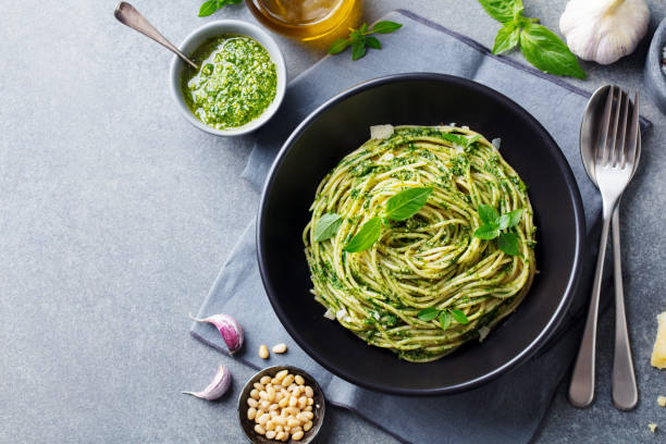 pasta spaghetti with pesto sauce and fresh basil leaves in black bowl. grey background. copy space. top view. - basil bowl cooked cheese imagens e fotografias de stock