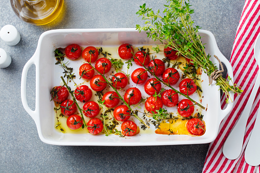Roasted cherry tomatoes with herbs in baking dish. Grey background. Top view.