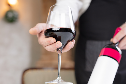 Sommelier holding glass of wine and bottle at restaurant.