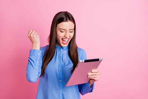 Photo of screaming shouting rejoicing overjoyed, girlfriend seeing sales started on her tablet held with her hands wearing blue shirt isolated over pink pastel color background