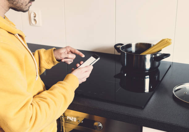 Home control, Man with mobile phone is setting induction hob Man with mobile phone in hand thanks to smart home control mobile application is setting induction cooker, home interior. cleaning stove domestic kitchen human hand stock pictures, royalty-free photos & images