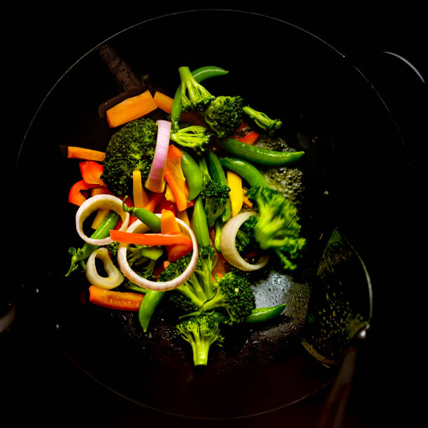 remuer la friture et faire sauter une variété de légumes frais colorés du marché dans un wok chaud. - poêle verte photos et images de collection