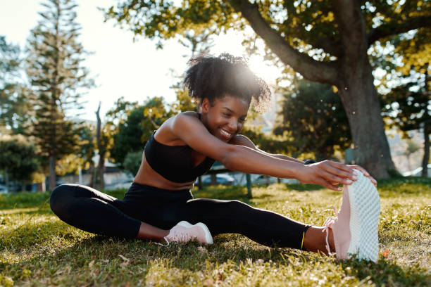 公園で彼女の足を伸ばす芝生の上に座っているスポーティフィットアフリカ系アメリカ人の若い女性の笑顔の肖像画 - 幸せな若い黒人女性が実行する前に彼女の筋肉を温める - running jogging african descent nature ストックフォトと画像