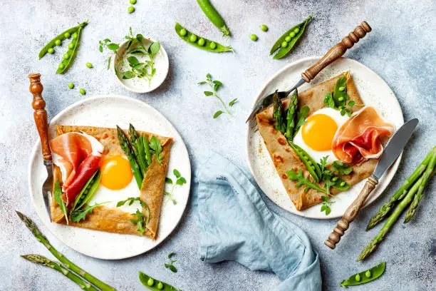 Photo of Buckwheat crepes, galette bretonne with asparagus, egg, green pea, jambon or prosciutto. Galette sarrasin, french brittany cuisine