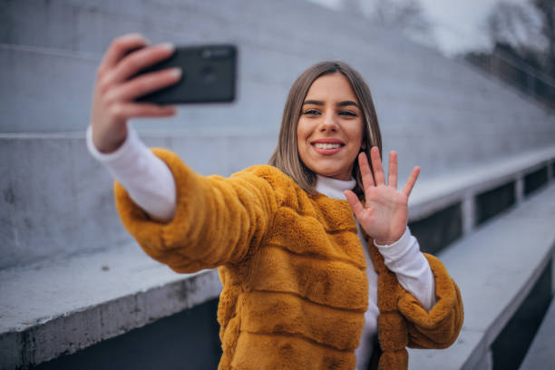 istock Young woman sitting on the stairs and making selfie 1205512072