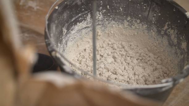 istock Construction worker man stirs the mixture in the bucket construction for alignment and putty walls of the apartment with the help of a powerful drill. Bucket with dry mortar for plastering the wall in the apartment 1205512460