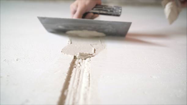 istock Worker aligns the wall with a spatula. Worker aligns the wall with construction putty. a close shot at the builder hands, who level the wall with a long spatula and plaster, the man applies the composition on the surface 1205513234