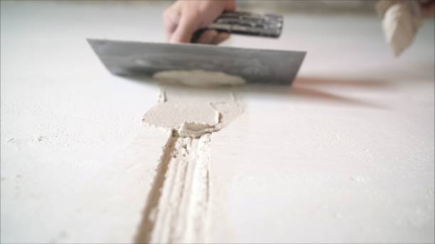 Worker aligns the wall with a spatula. Worker aligns the wall with construction putty. a close shot at the builder hands, who level the wall with a long spatula and plaster, the man applies the composition on the surface stock photo