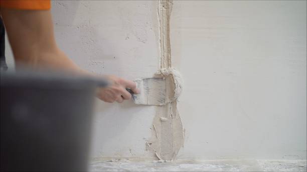 istock Worker using the trowel for plastering the concrete wall at the construction site. Making the smoothness and flat the surface of cement wall by wooden trowel. Labor day. Worker smoothes a wall using building plaster 1205513267