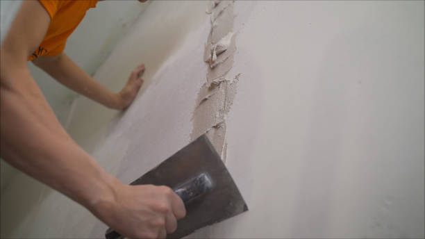 istock Worker using the trowel for plastering the concrete wall at the construction site. Making the smoothness and flat the surface of cement wall by wooden trowel. Labor day. Worker smoothes a wall using building plaster 1205513273