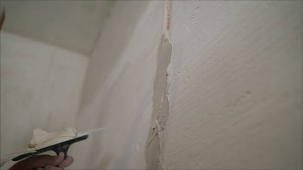 istock Worker aligns the wall with a spatula. Worker aligns the wall with construction putty. a close shot at the builder hands, who level the wall with a long spatula and plaster, the man applies the composition on the surface 1205513313