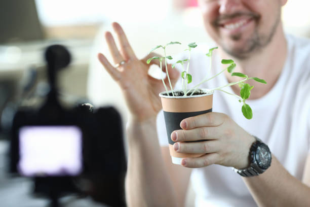Male video blogger hold pot with green sprouts