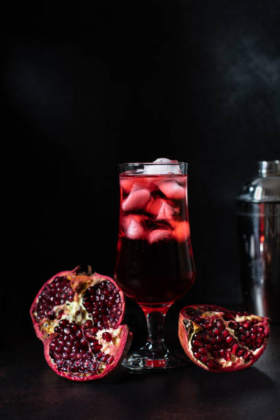 istock Glass with a pomegranate drink and a cocktail shaker. Pomegranate cocktail. Refreshing pomegranate juice with ice. Sliced Pomegranate. Dark background, vertical, copy-space 1205535033