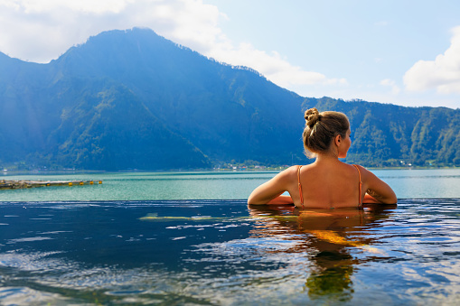 Young woman relax in infinity pool with lake view. Natural hot spring spa under Batur volcano. Travel in Kintamani, Bali. Healthy lifestyle, recreational activity on family summer holiday.