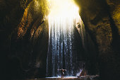 Woman meets sunrise in the cave under the big waterfall on Bali island, Indonesia