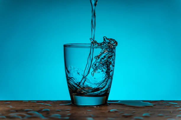 水は水のボトルからガラスに流れ込む - 青い背景 - overflowing water glass bottle ストックフォトと画像