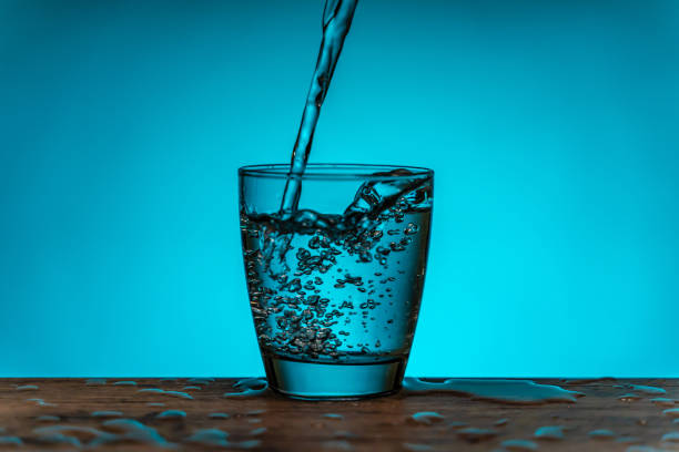 水筒から水ガラスを注ぐ - 青い背景 - overflowing water glass bottle ストックフォトと画像