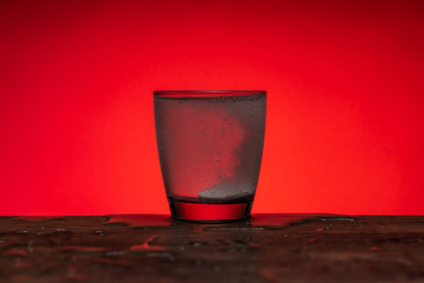 istock Effervescent pill dissolving into glass of water - red  background 1205537272