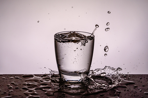 Raindrops fall in glass full with water - white background. The scene is located in a studio environment. The footage is taken with Sony A7III camera