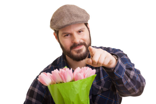 白い背景に孤立したピンクのチューリップの花束を持つ尖った人差し指を持つひげを生やした若いハンサムな男。母の日、バレンタインデー、イースターと驚きのコンセプト。 - single flower flower mothers day easter ストックフォトと画像