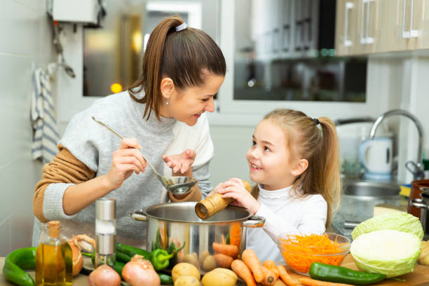Positive mother and little daughter tasting soup together Positive mother and little daughter tasting soup together at home family dinners and cooking stock pictures, royalty-free photos & images