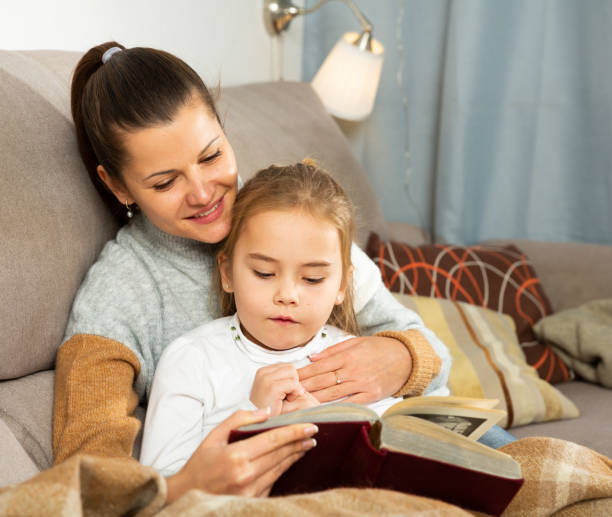 istock Young woman reading an interesting book with daughter 1205540495