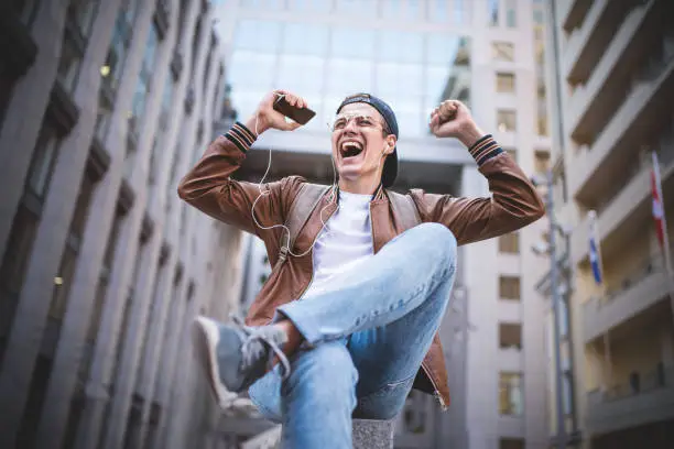 Photo of Happy man listening to music with headphones from a smartphone on the street.