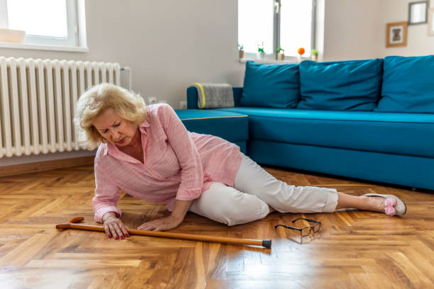 donna in pensione indifesa con i capelli biondi seduti sul pavimento a casa. i rischi che derivano dall'invecchiare. - falling people tripping senior adult foto e immagini stock