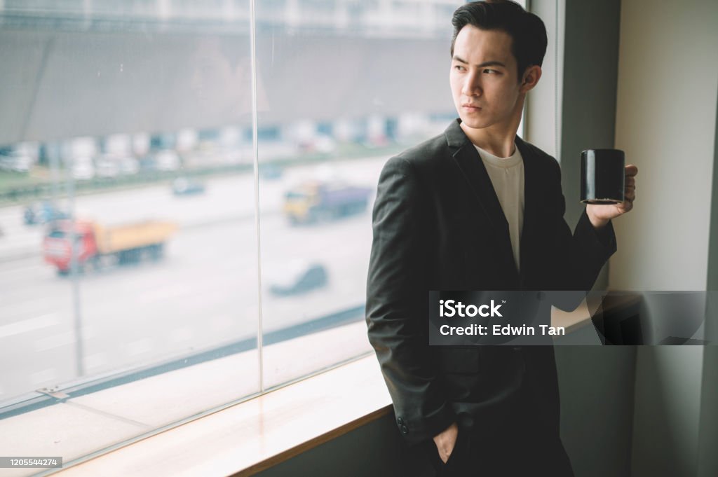 an asian chinese young white collar worker holding a coffee cup while looking outside the window Men Stock Photo
