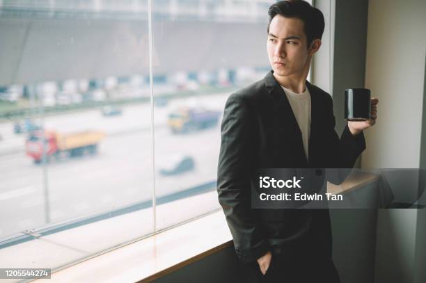 An Asian Chinese Young White Collar Worker Holding A Coffee Cup While Looking Outside The Window Stock Photo - Download Image Now