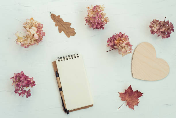 Workspace with notebook on white background. Autumn composition with dry flowers and leaves. Flat lay, top view.