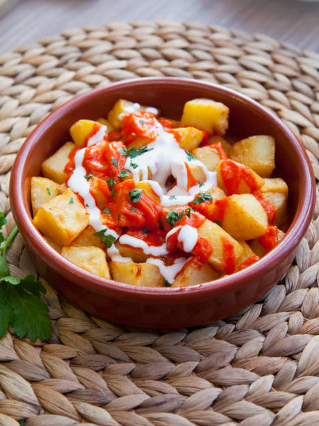 Spanish cuisine potato snack - potato bravas. Spanish cuisine potato snack with tomato and white sauce -  patatas bravas, served in the red terracotta dish. patatas bravas stock pictures, royalty-free photos & images