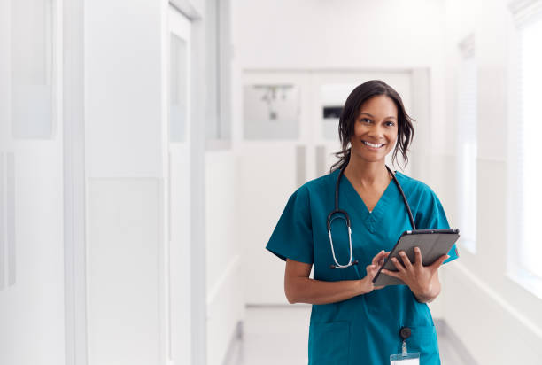 portret uśmiechniętej kobiety lekarz noszenia zarośla w szpitalu korytarz holding digital tablet - surgeon medical instrument expressing positivity looking at camera zdjęcia i obrazy z banku zdjęć