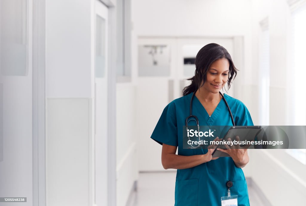 Female Doctor Wearing Scrubs In Hospital Corridor Using Digital Tablet Healthcare And Medicine Stock Photo