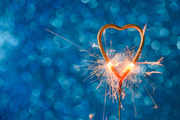 istock Burning sparkler heart shaped on blue bokeh background 1205549503