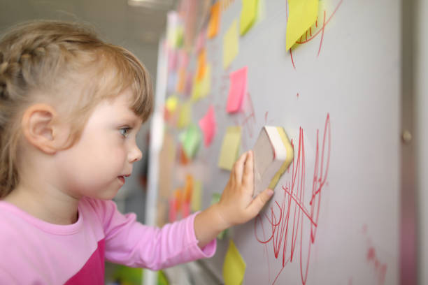 Little girl erases lettering Close-up view of kid washes off the board in class with sponge. Child wiping doodle written on chalkboard. Many sticky notes on whiteboard. Childhood concept kids using smart board stock pictures, royalty-free photos & images