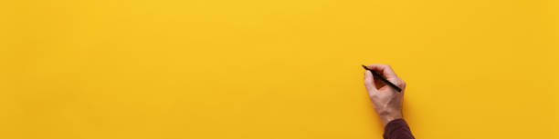 istock Male hand about to write on blank yellow background 1205550707