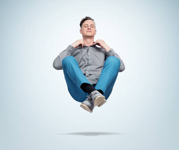 hombre feliz con ropa casual cerrando los ojos meditando levitando en el aire. relajación comprensida - levitación fotografías e imágenes de stock